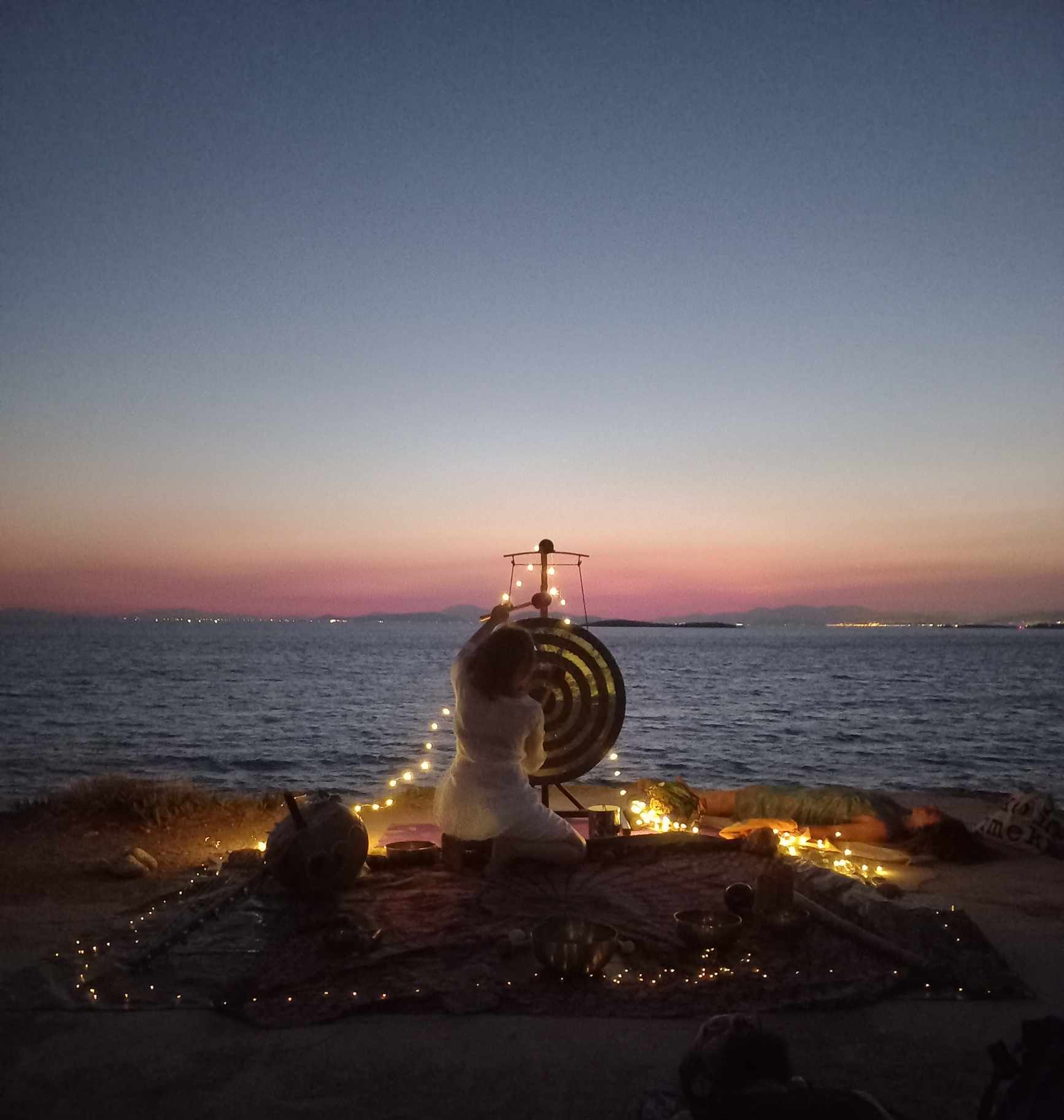 H Χριστίνα Αντωνιάδου παίζει γκονγκ σε ηχόλουτρο στην παραλία κατά τη διάρκεια της ηλιοβασιλέματος